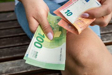 Close-up of woman holding euro banknotes in hands while sitting outdoors, counting money cash