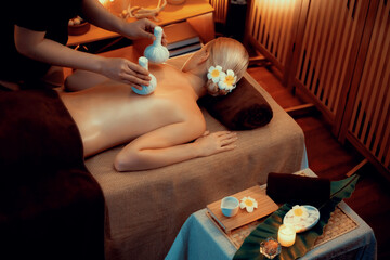 Hot herbal ball spa massage body treatment, masseur gently compresses herb bag on woman body....