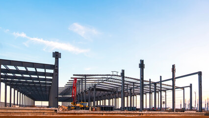 Fototapeta premium Metal structure of factory industrial building framework with crane truck on the ground in construction site area against blue evening sky background