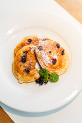 Fluffy pancakes topped with blueberries and syrup on a white plate