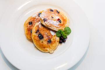 Fluffy pancakes topped with blueberries and syrup on a white plate