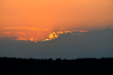 The setting sun in summer. The sun circle and the forest on the horizon.  The sun goes behind a cloud in the evening.