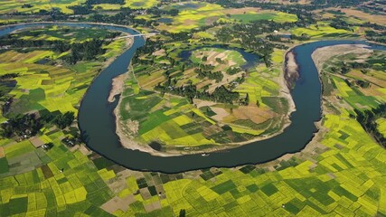 Bogura, Bangladesh - 21 August 2025: Aerial view of a winding river flowing through vibrant agricultural land, creating a stunning contrast of colors and textures.