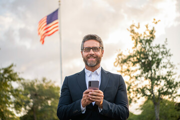 Businessman using phone at American flag. Man with phone outdoor. Hispanic business man with phone. Business communication. Casual business man chatting on phone outdoor