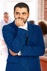 Man in professional attire appears to be contemplating something important, set in an office environment. His pensive expression conveys deep thoughtfulness and decision-making in a corporate context.
