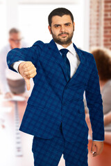 A business professional in a formal suit gesturing a thumbs-down, conveying disapproval or disagreement in a modern office environment. Perfect for representing rejection, criticism, or dissatisfactio