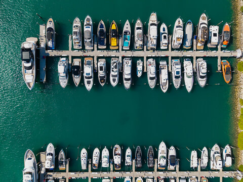 Aerial view of luxury yachts docked at marina. Top-down drone shot of yachts. Boats and sailboats line the scenic seashore. Yacht cruising along the coastline. Harbor filled with vessels at dawn.