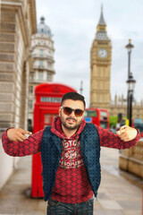 Man in fashionable attire posing in front of the iconic London telephone booth and Big Ben. Highlights urban style, fashion, and classic London landmarks.