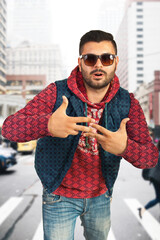 Young fashionable man stands on a city street, expressing cool and confident attitude. Shows modern urban style while conveying bold personality through striking hand gestures and stylish outfit.