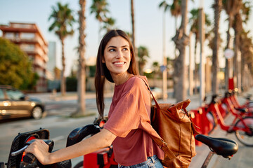 Smiling happy beautiful woman using mobile phone to unlock electric bicycle in city
