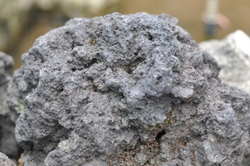 A large rock with a rough surface. The rock is grey and black in color. It is a piece of lava or a rock that has been weathered by the elements