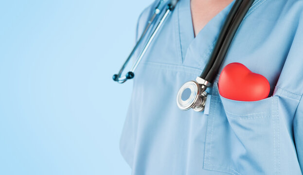 Male doctor cardiologist holding red heart in pocket of surgical suit and phonendoscope on grey background. Doctor care heart health concept. World Hypertension or donor Day.