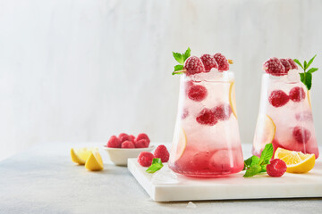 Spring or summer cold refreshing raspberry and lime cocktail garnished with mint and thyme leaves in a glass on a light background. Summer Drinks for home.
