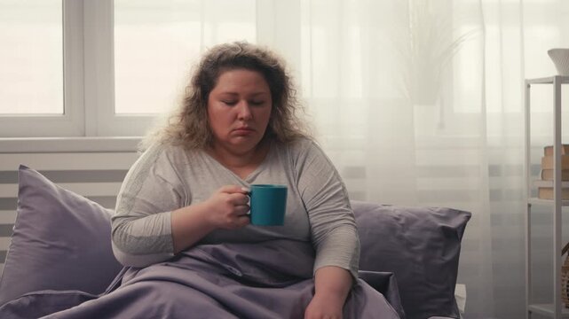 Exhausted middle-aged woman drinking coffee in bed, suffering lack of sleep
