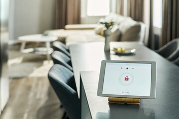 Tablet displaying security lock screen standing on kitchen counter in modern home interior, sunlight streaming through window, living room with sofa and table visible in background