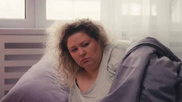 Sad plus size woman lying in bed in morning, migraine from weather sensitivity