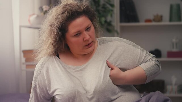 Unhappy middle-aged woman feeling sharp chest pain on bed, heart failure risk