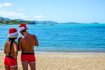 Fototapeta na wymiar Couple in Santa Hats Celebrating Christmas on a Tropical Beach. Concept of Holiday Travel, Seasonal Celebration, and Love in Paradise.