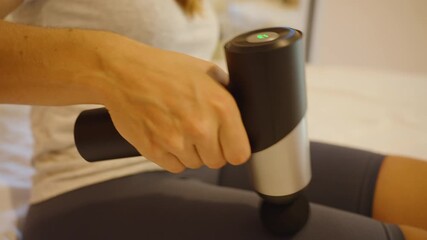 Woman using massage gun on thigh, close up, muscle recovery concept