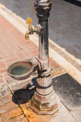 Obraz premium The antique water fountain stands proudly on a brick walkway, with crystal-clear water collecting in its basin. Sunlight illuminates the surrounding foliage, creating a peaceful atmosphere