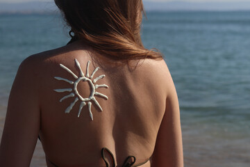 Sun image made with sunscreen on woman's back. Sunbathing on the beach. Close-up. Woman in swimsuit on the beach, back view. Using sunscreen. Concept of beach vacation, seaside resort, beach holiday