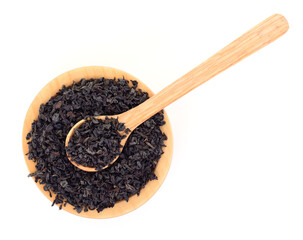 Wooden bowl with dry black tea leaves and spoon isolated on white background