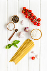 Spaghetti with ingredients for cooking Italian pasta - tomatoes and basil with garlic - on a white wooden background, top view. Flat lay