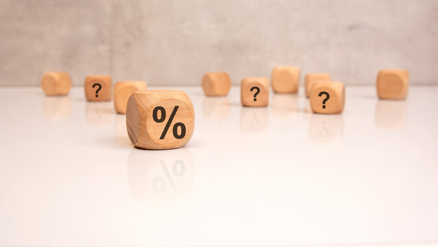 Wooden cubes with percent sign and question marks, concept of uncertainty in finance.