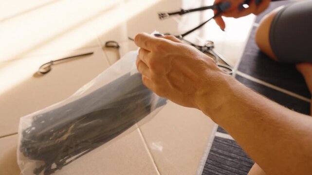 Close up of hands holding black cable ties above open plastic bag, equipment sorting concept