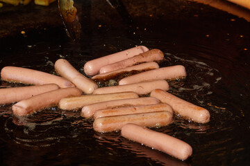 Fototapeta premium Sausages are fried in oil in a large frying pan