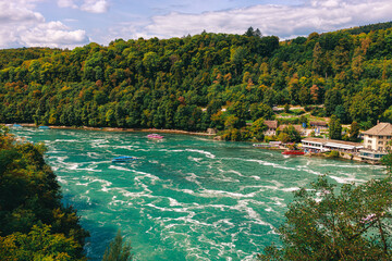 Majestic view of Rhine Falls, the largest waterfall in Europe, located near Schaffhausen in northern Switzerland. Powerful cascades of water rush over rugged rocks, surrounded by lush greenery and mis © Breg