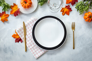 Festive Thanksgiving table setting with pumpkins and plate, cutlery and napkin - autumn leaves and tableware decorated on gray background, flat lay. Top view