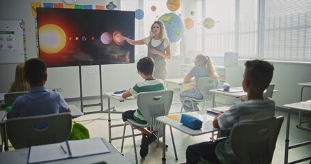 Astronomy Class: Female Teacher Explaining Solar System to Primary School Children Using Digital Screen. Group of Young Boys and Girls Sitting at the Desks, Learning Space Science in Modern Classroom.
