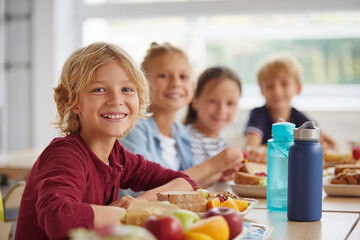 Children enjoying healthy lunch together at school cafeteria. Balanced meals with fruits, sandwiches, and water