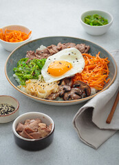 Bibimbap, authentic korean dish with a steamed rice topped with fried egg, beef, colorful vegetables, traditional dish of Korea on light background with chopsticks
