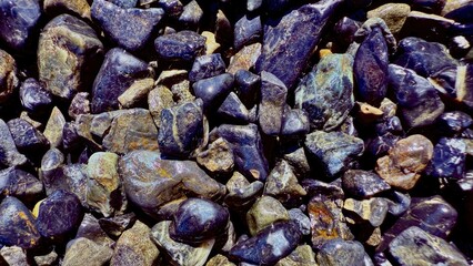 glossy wet river stones with deep purple and earthy brown tones creating natural textured pattern for background or design element