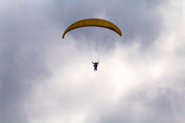 Small silhouette of an adult paragliding with a cloudy sky in the background, in Valle de Bravo, State of Mexico