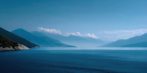 Fototapeta premium Tranquil lake with misty mountains and clear blue sky at sunrise