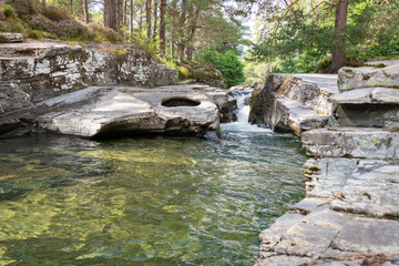 Naklejka premium A wide shot with long-exposure photo of the Linn of Quoich waterfall under Scots Pine trees.