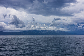 Stormy sky over mountains and sea. Dark dramatic clouds hang over the water surface, creating an atmosphere of tension and grandeur of nature. Podaca village, Makarska Riviera, South Dalmatia, Croatia