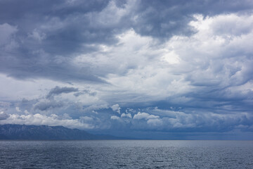 Obraz premium Stormy sky over mountains and sea. Dark dramatic clouds hang over the water surface, creating an atmosphere of tension and grandeur of nature. Podaca village, Makarska Riviera, South Dalmatia, Croatia