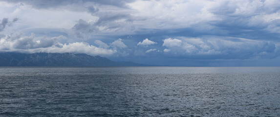 Stormy sky over mountains and sea. Dark dramatic clouds hang over the water surface, creating an atmosphere of tension and grandeur of nature. Podaca village, Makarska Riviera, South Dalmatia, Croatia