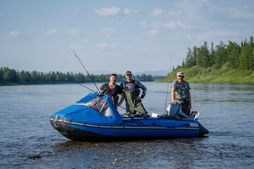 Three happy fishermen in a boat with spinning rods on a river near a forest