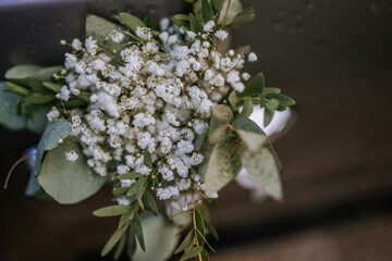 Close-up of a delicate white baby&rsquo;s breath flower bouquet with eucalyptus leaves, decorated on a car door handle, with visible raindrops on petals and leaves.