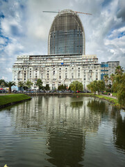 Batumi, Georgia &ndash; White Magnolia building and unfinished skyscraper with crane above, reflected in lake water under dramatic cloudy sky. Iconic architecture and modern cityscape of Batumi.

