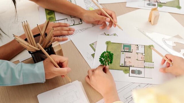Architect and engineer use tree model discuss about building blueprint on table with architectural document, measurement tools and wooden block scatter around at modern office. Closeup. Delineation.