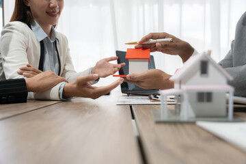 Real estate agent presenting a house model to client during a meeting, discussing property purchase terms and investment opportunities in a professional setting