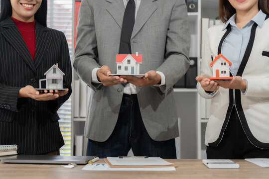 Real Estate Harmony: Professionals with diverse appearances showcase miniature homes, representing a sense of harmony, unity, and collaboration in the property market. - Powered by Adobe