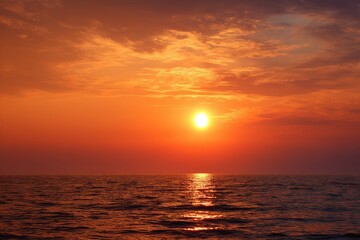 Obraz premium Fiery sunset over calm ocean; orange and purple hues dominate the sky, reflecting on the water's surface