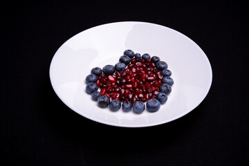 Heart shaped blueberries with pomegranate in the middle on white plate with isolated background